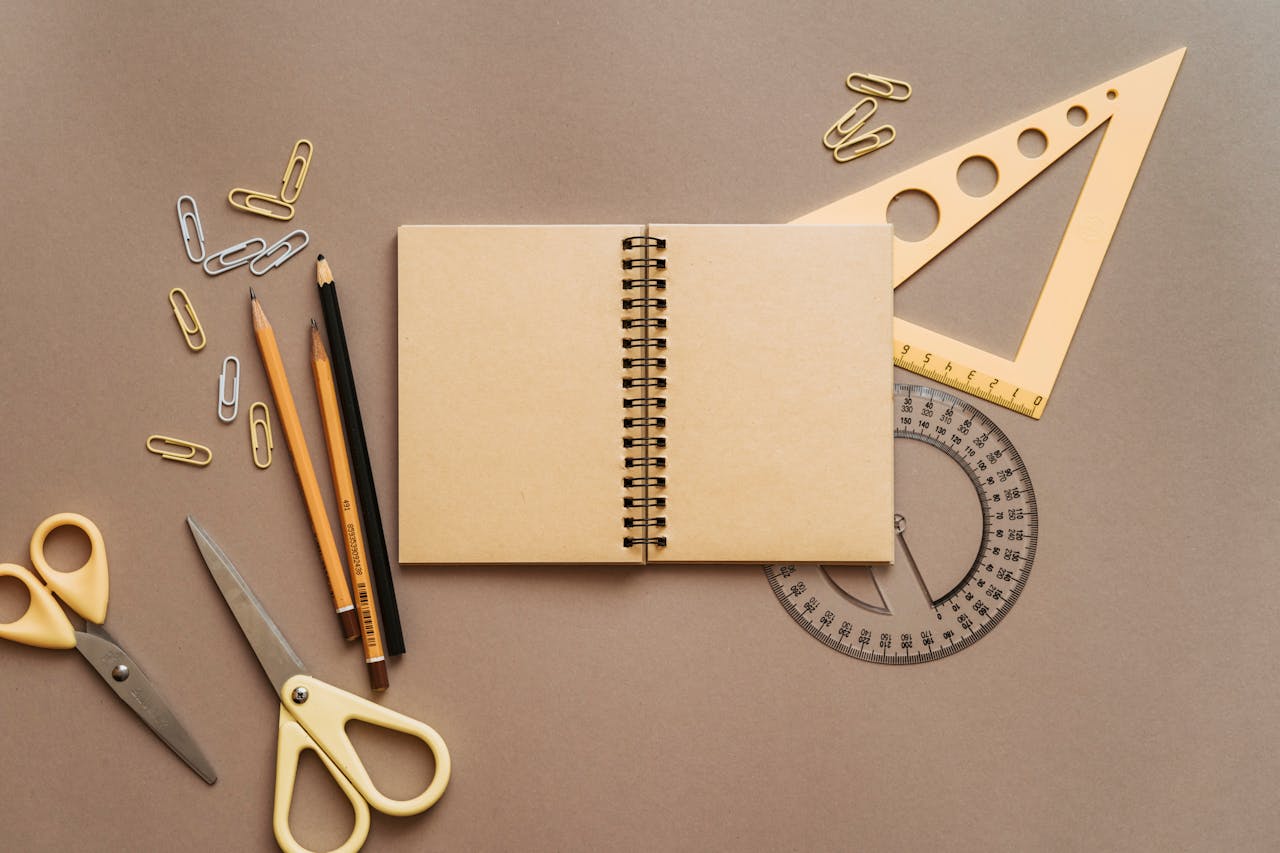 Flat lay of school supplies featuring a spiral notebook, scissors, and stationery on a brown background.